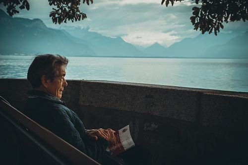 man sitting while holding a book watching on body of water