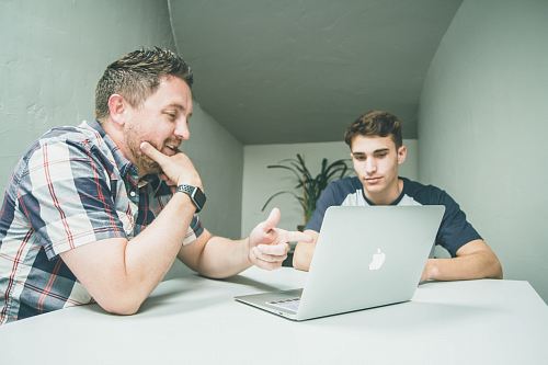man wearing white and black plaid button-up sports shirt pointing the silver MacBook
