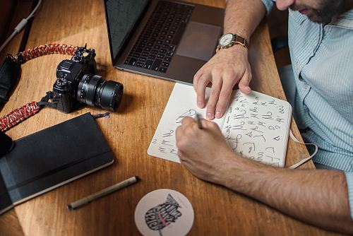 man writing on paper in front of DSLR