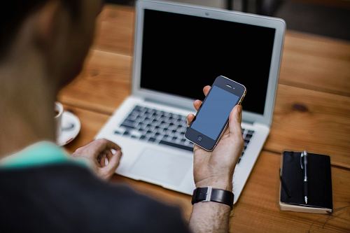 person holding black iPhone 4 front of MacBook Air