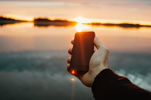 person holding black iPhone near lake during sunset