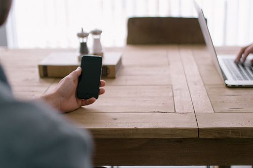 person holding smartphone in front of brown table