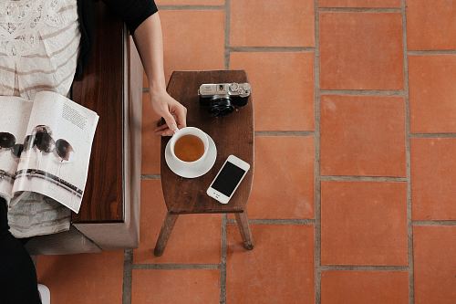 person sitting on sofa while reading brochure holding teacup