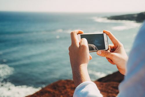 person standing on cliff taking photo of body of water during daytime