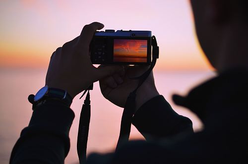 person taking photo of sunset using compact camera