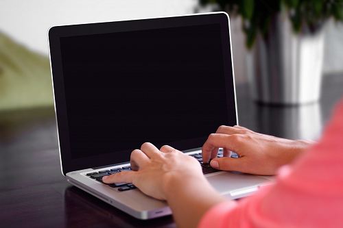 person wearing pink shirt typing on gray laptop computer on desk