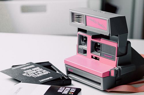 pink and gray Polaroid instant camera on white wooden surface