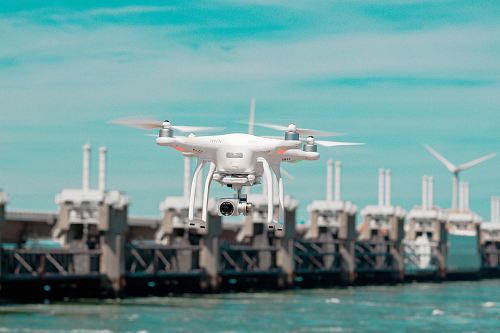 selective focus photography of white drone hovering above body of water