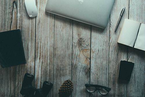 silver MacBook, ballpoint pen, binoculars, eyeglasses arranged in circular pattern