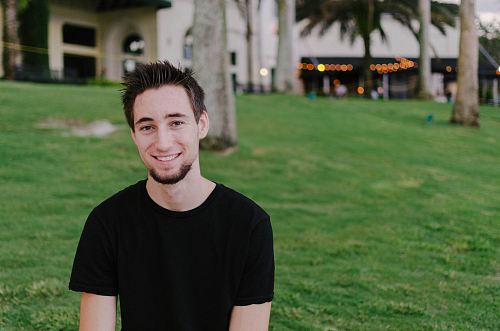 smiling man in black shirt standing near trees