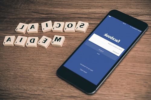 space gray iPhone 6 with Facebook log-in display near Social Media scrabble tiles