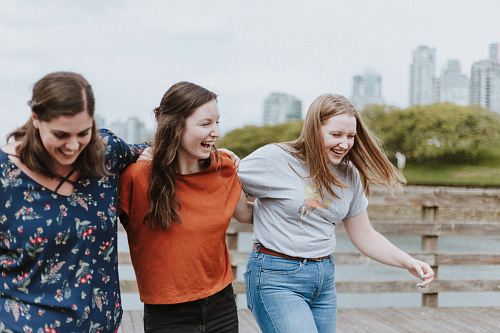 three women walking on brown wooden dock near high rise building during daytime