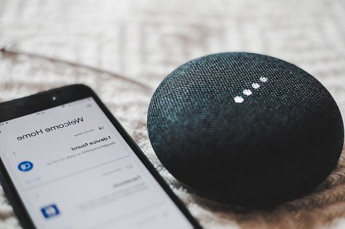 turned-on charcoal Google Home Mini and smartphone