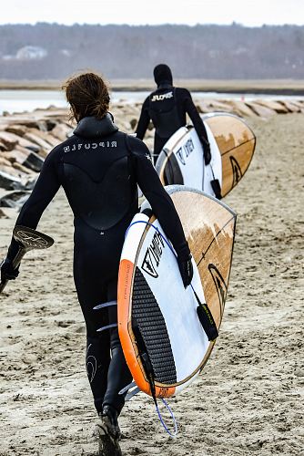 two person walking towards body of water while carrying surfboards
