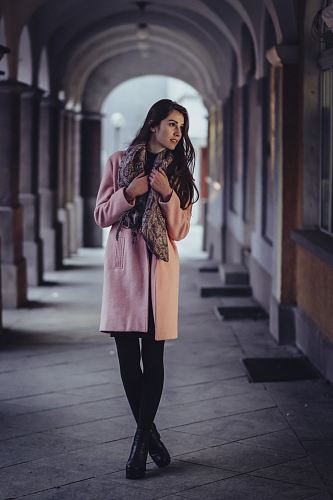 woman holding scarf with cross legs in between of gray concrete wall