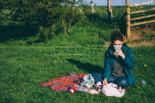 woman in blue outfit using blue smartphone while sitting on grass