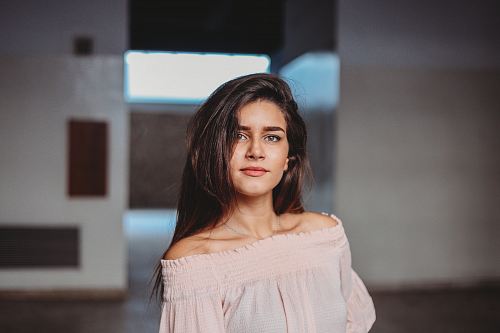 woman in nude off-shoulder shirt standing beside concrete wall selective focus photography