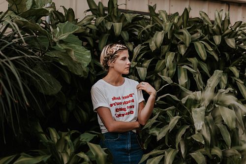 woman in white shirt standing and surrounded by green plants