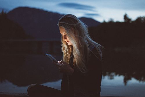woman looking at phone beside body of water