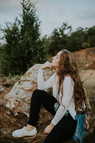 woman sitting on rock near green tree under white clouds and blue sky