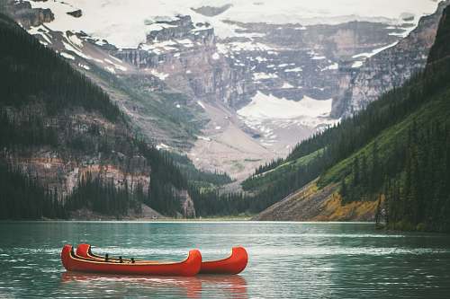 mountain two orange boats on body of water in front of mountain with trees during daytime canoe