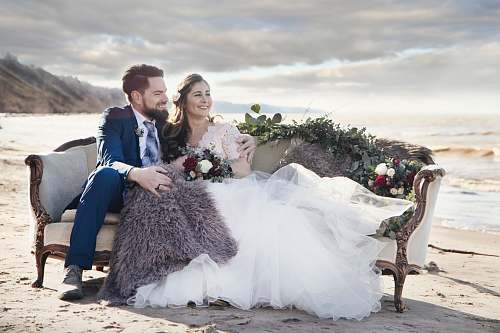 clothing man and woman sitting on padded sofa beside sea human