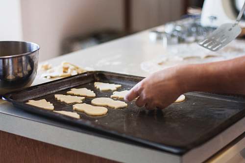 food person lining assorted-shaped cookies on baking sheet inside kitchen bake