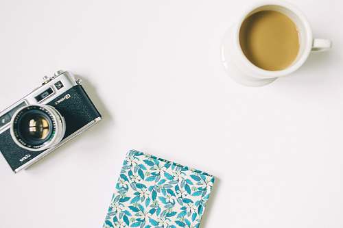 desk black and grey SLR camera, floral notebook, and white ceramic mug camera