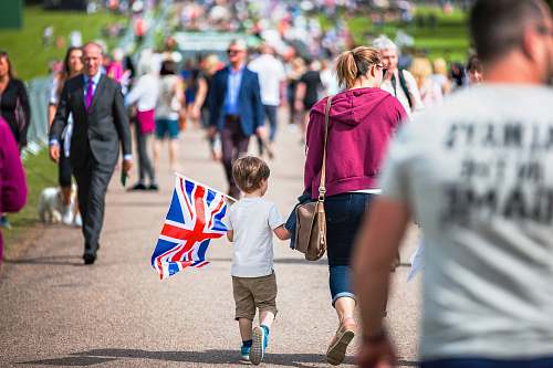 person selective focus photography of boy holding U.K. flag walking on pathway full of people human