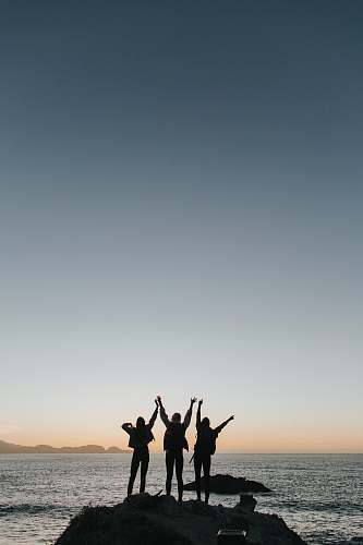 grey silhouette photography of persons raising hands while standing on island sea