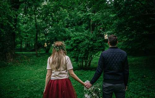 human woman and man standing holding hands facing trees back