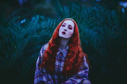 human photography of red-haired woman standing near leafed plants people