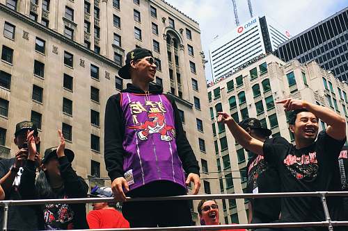 human smiling \Jeremy Lin in Raptor uniform atop of vehicle by men during daytime downtown