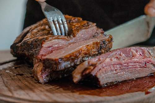 food person slicing a meat on brown wooden board bbq
