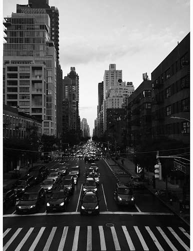 city grayscale photography of people walking on pathway near buildings and different vehicles on road road