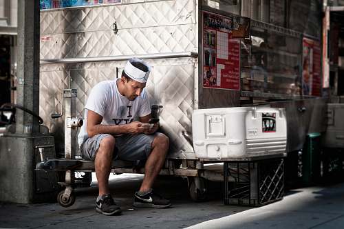 person man in white shirt holding smartphone sitting near chest cooler people