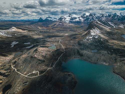nature aerial photography of lake surrounded with mountains under cloudy sky outdoors