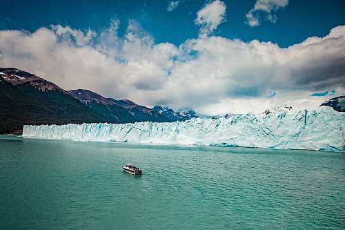 ice aerial photography of white boat on body of water beside ice block cliff during daytime mountain