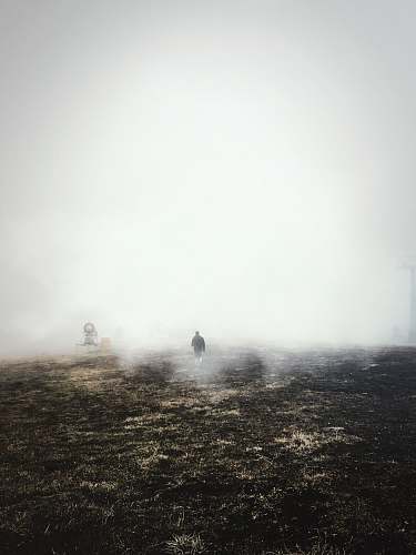 fog man in black jacket walking on brown field with mist at daytime weather