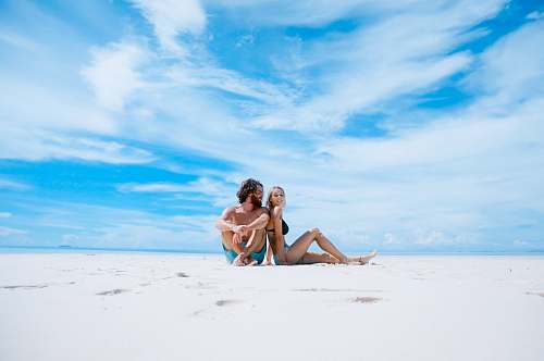 beach man sitting beside of woman in black bikini top clothing