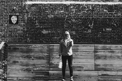 black-and-white person standing beside wall brick
