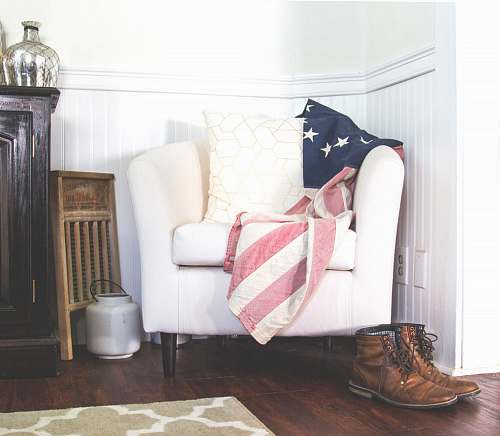 american US flag and white throw pillow on white fabric sofa chair in room interior