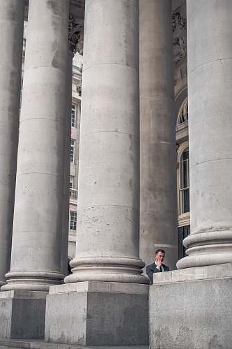 pillar man standing beside gray concrete pillars grey