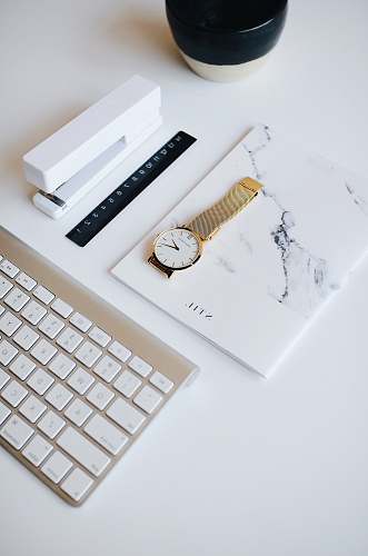 office watch on top of book beside stapler near Apple keyboard design