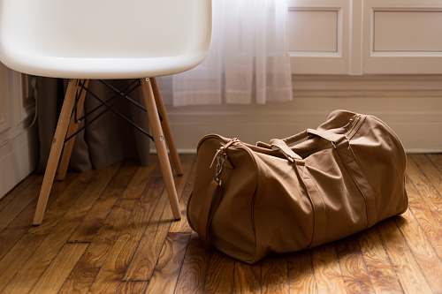 bag brown duffel bag beside white and brown wooden chair wood