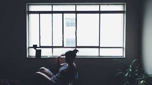 flora woman sitting on chair beside glass window near plant jar