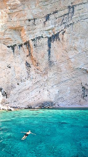 man floating over body of water near rock formation