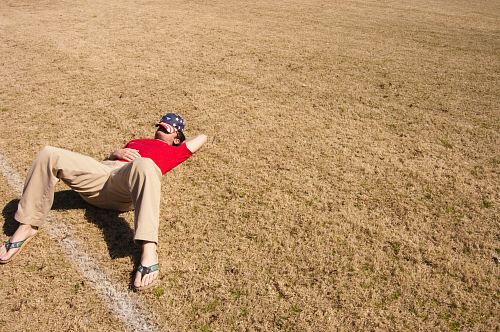 man in red top lying on lawn field during daytime