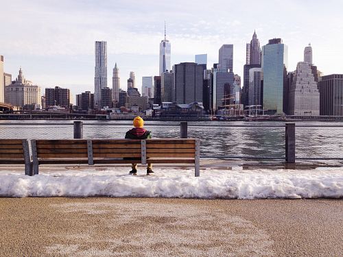 person in knit cap sitting on wooden bench in front of body of water during daytime