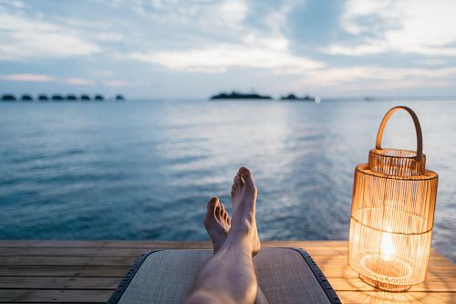 person lying on chair and facing on body of water